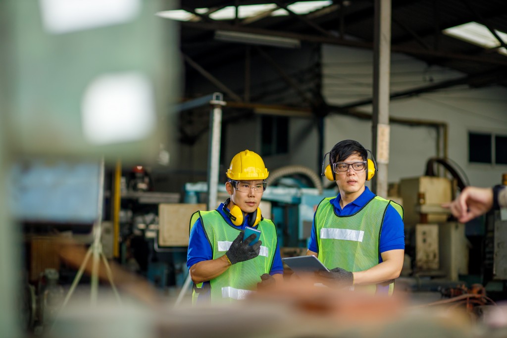 Two asian maintenance engineers discuss inspect relay checking information and protection system on a tablet computer in a factory. They work a heavy industry manufacturing factory.