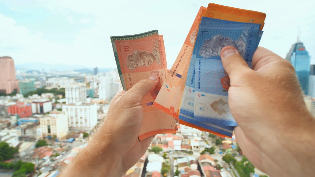 A young man recounts in his hands the money of Malaysia against the background of the city center of Kuala Lumpur
